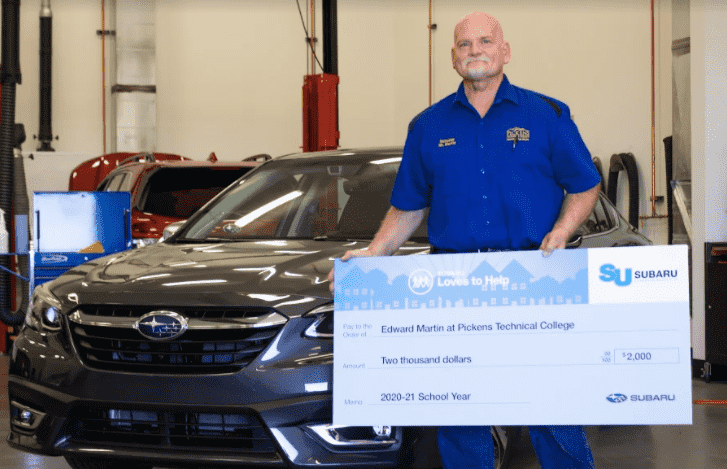 Man standing in front of the car and holding cheque with amount $2000