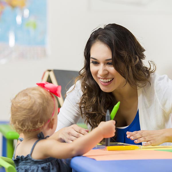 daycare teacher helps toddler with coloring project