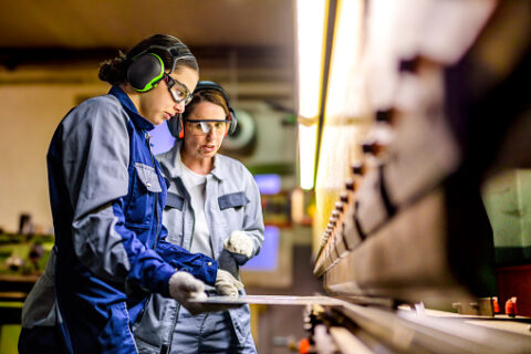 Two focused women in safety gear working diligently in an advanced manufacturing facility.