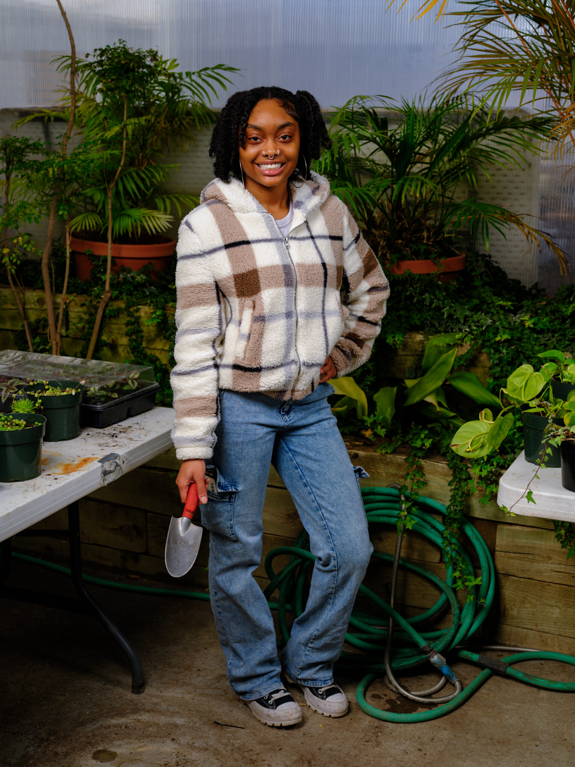 Person holding a garden trowel among plants in a greenhouse